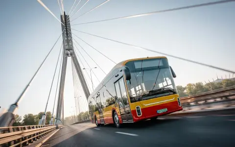 Żółto-czerwony autobus elektryczny Yutong U12 jedzie po moście nad rzeką.