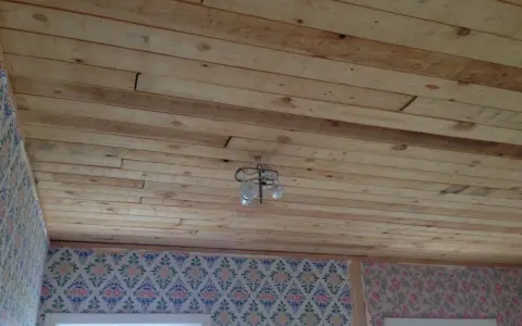 Taket av obehandlad furu inomhus är redo att målas. En taklampa hänger från träpanelen.