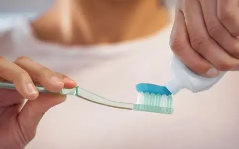 Nakładanie niebieskiej pasty do zębów z fluorkiem sodu na szczoteczkę.