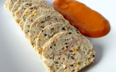 Fiambre de pollo casero en rodajas, con trocitos de verdura y jamón, acompañado de una salsa naranja.