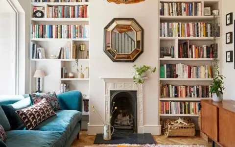 Acogedor salón estrecho y rectangular con sofá azul, chimenea y estanterías repletas de libros.