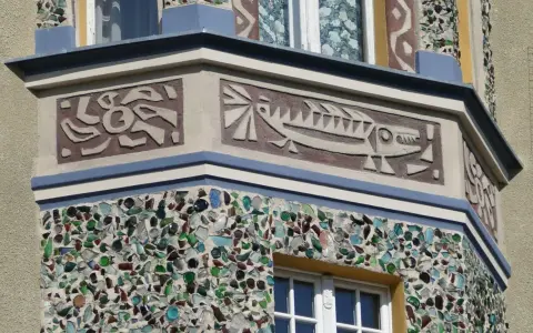 Fasada ozdobiona mozaiką z kolorowego szkła i sgraffito z motywem ryby.