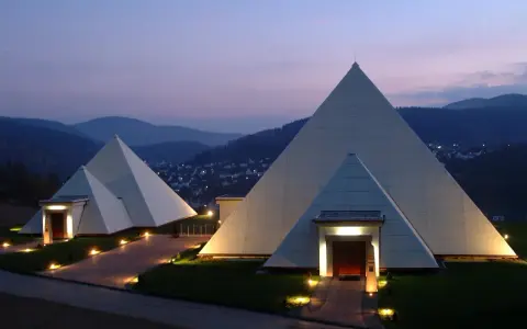 Zwei moderne Pyramiden im Sauerland, beleuchtet im Abendlicht, mit einem Dorf im Hintergrund.