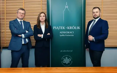 Trzy osoby w garniturach stoją przed zielonym banerem kancelarii "Piątek Królik Adwokaci".