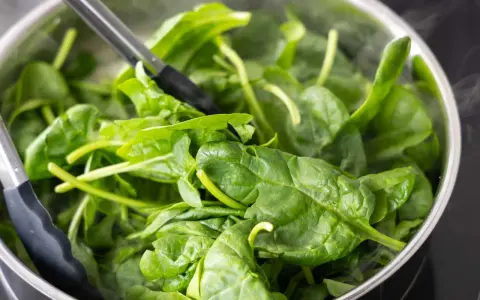 Szpinak w garnku, gotowy do dalszej obróbki, aby dowiedzieć się, jak mrozić szpinak. Para unosi się znad liści.