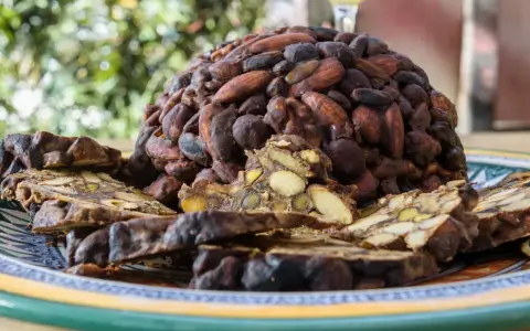 Un pan pepato a forma di cupola, ricoperto di mandorle e cacao, con fette tagliate che rivelano frutta secca e spezie.