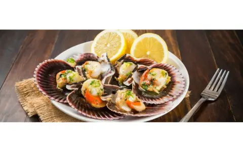 Zamburiñas a la plancha servidas en sus conchas, adornadas con perejil picado y rodajas de limón. Un plato delicioso y fresco.