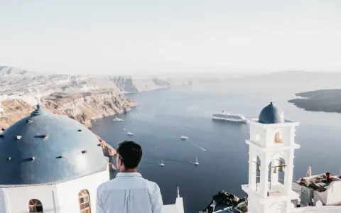A man gazes at the caldera on a gay Greek island, with iconic blue domes and white architecture overlooking the Aegean Sea.
