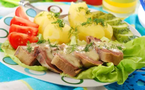 Kawałki ozorków w sosie chrzanowym, podane z ziemniakami, pomidorami i ogórkiem kiszonym. Danie ozdobione jest świeżym koperkiem.