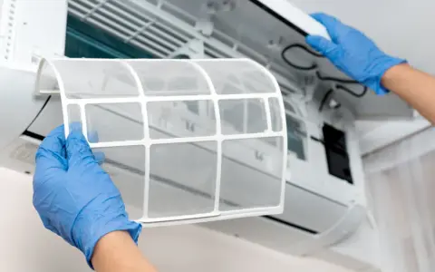 Mani guantate rimuovono il filtro del condizionatore per pulirlo. Un passo essenziale per un'aria fresca e pulita.