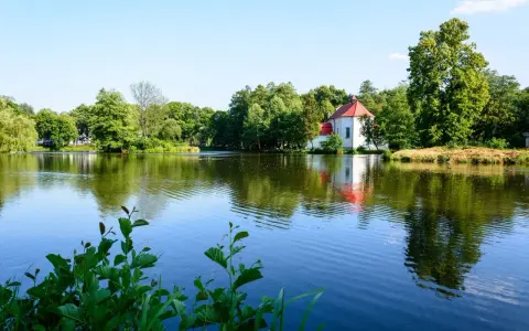 Malowniczy kościół na wodzie w Zwierzyńcu, otoczony zielenią i odbijający się w spokojnej tafli jeziora.