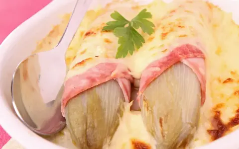 Deux endives braisées enveloppées de jambon, nappées de fromage fondu et gratiné, garnies d'une feuille de persil. Un plat réconfortant.