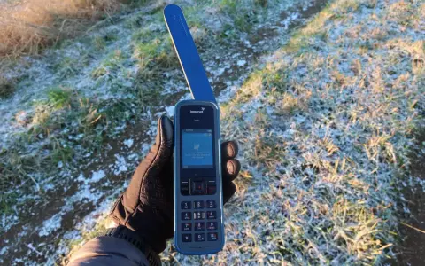 Ręka w rękawiczce trzyma telefon Inmarsat IsatPhone, gotowy do nawiązania połączenia przez telefonię satelitarną w mroźny poranek.