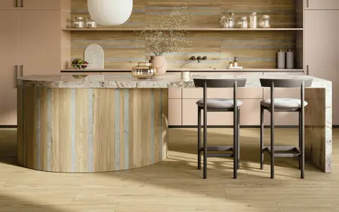 Interni di una casa super moderna: isola cucina in legno e marmo, sgabelli grigi, mobili rosa cipria e pavimento in parquet chiaro.