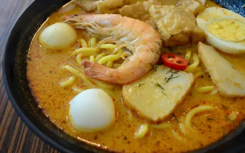 Eine Schüssel Laksa, ein beliebtes Singapur-Essen, mit Garnelen, Ei, Tofu und Nudeln in cremiger Kokosbrühe.