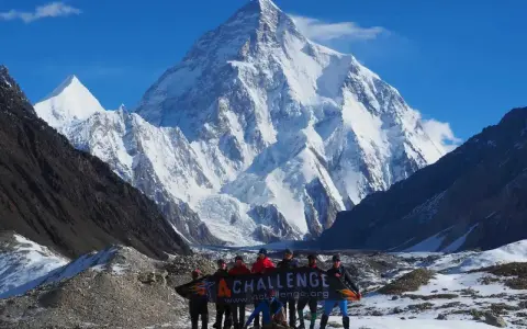 Grupa ludzi z banerem przed majestatycznym szczytem K2 w Karakorum. To wyzwanie w górach Pakistanu.