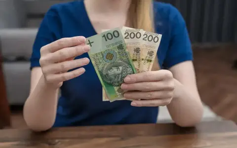 Dłonie trzymają polskie banknoty: 100 zł i dwa razy po 200 zł. To może być część zasiłku rodzicielskiego.