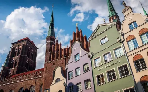 Kolorowe kamienice w Gdańsku pod błękitnym niebem z chmurami, w tle kościół.
