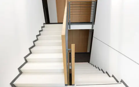Nowoczesne schody z jasnymi stopniami i drewnianą balustradą. Każdy podstopnica jest wyraźnie zaznaczona.