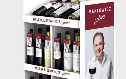 Regał z butelkami wina, z etykietami "Makłowicz poleca" i zdjęciem Roberta Makłowicza.