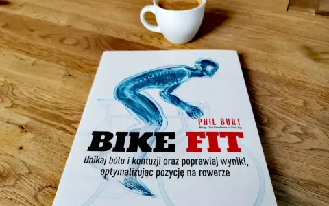 Książka "Bike Fit" z anatomicznym schematem rowerzysty i filiżanką kawy na drewnianym blacie.