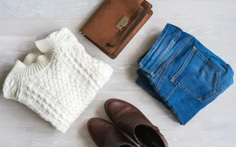 En vit kabelstickad tröja, jeans, bruna stövlar och en brun handväska. Perfekt för en kapselgarderob lista.