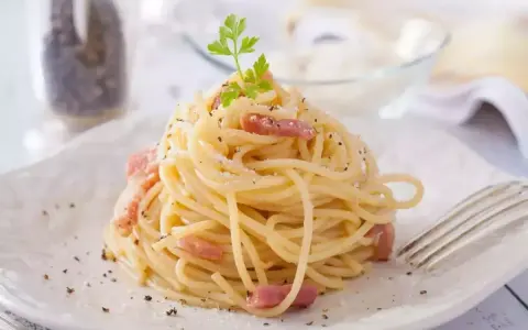 Un plat de tagliatelles carbonara crémeuses, garni de lardons et de persil frais, prêt à être dégusté.