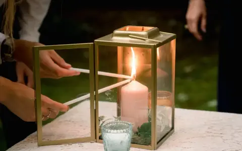Manos encienden velas finas de una vela principal dentro de un farol dorado. Una escena de la ceremonia de las velas.