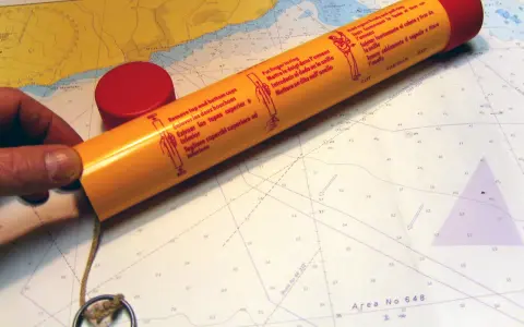 Seenot-Leuchtrakete mit roter Kappe und Anleitung auf einer Seekarte.