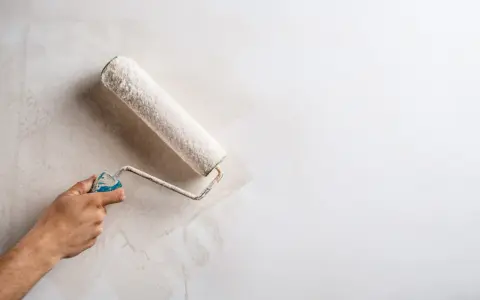 Main d'une personne appliquant une couche de peinture sur un mur déjà peint avec un rouleau.