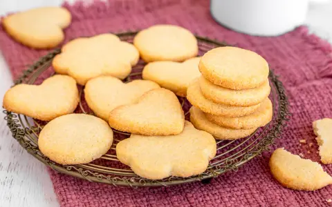 Deliziosi dolci da fare in casa, biscotti a forma di cuore e fiori su un vassoio di metallo, adagiati su un panno color prugna.