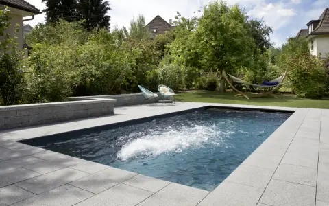 Aménagement paysager d'une piscine creusée avec terrasse en pierre, deux chaises bleues et un hamac invitant à la détente.