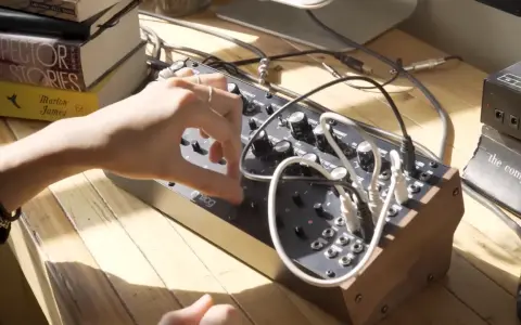 Ręka manipuluje pokrętłami na syntezatorze Moog DFAM, tworząc dźwięki.
