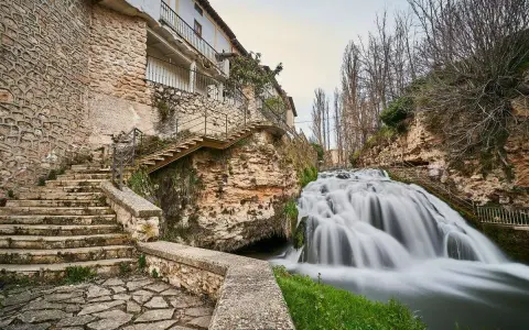 Escaleras de piedra y un caserío se funden con la cascada en la Alcarria Alta.