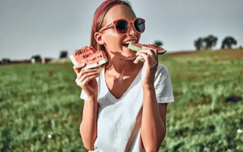 Dziewczyna w okularach zajada soczyste kawałki arbuza na tle zielonego pola. To idealny moment, kiedy jest sezon na arbuzy!