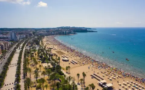 Tłum ludzi cieszy się słońcem na plaży, a w tle widać miasto. To idealne miejsce na wakacje, pełne atrakcji Costa Dorada.
