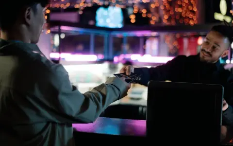 Un cliente entrega tarjetas a un camarero en un bar con luces de neón. Existe el derecho de admisión en los bares.