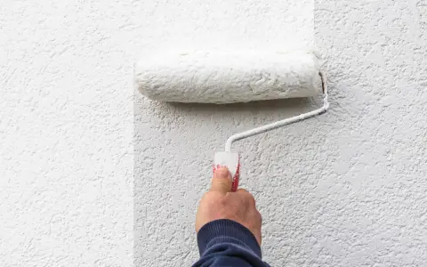 Hand rollt weiße Farbe auf eine strukturierte Wand. Man sieht, welche Wandfarbe am besten deckt.