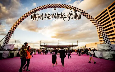 Gente camina bajo un arco con el letrero "When We Were Young Festival" sobre una alfombra rosa.