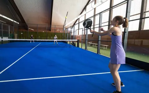 En kvinna i lila klänning spelar padel. Hon är redo att slå bollen på den blå banan.