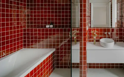 Salle de bain aux carreaux rouges vifs. La question "faut il carreler toute la salle de bain" se pose face à cette audace. Baignoire, lavabo et douche sont intégrés.