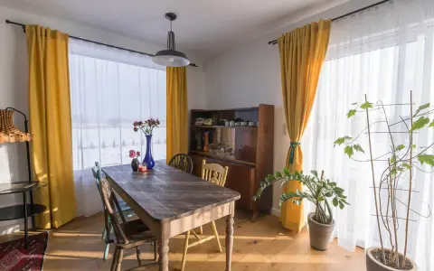 Słoneczne, żółte zasłony tworzą przytulny wystrój okien w stylu retro. Drewniany stół i kredens dodają ciepła.