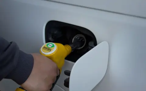 Ręka trzymająca żółtą dyszę dystrybutora, tankuje samochód. Na dyszy widnieje napis "DIESEL B10".