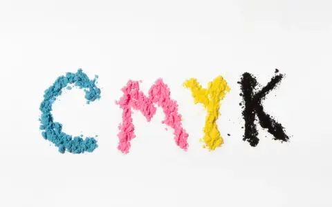 Litery CMYK ułożone z kolorowego proszku. Kolejność kolorów: cyjan, magenta, żółty, czarny.