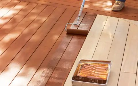 Aplicando protector para proteger madera exterior. Un rodillo extiende el líquido sobre las tablas de madera de una terraza.