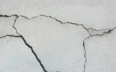 Pęknięcia na jasnej powierzchni betonu, świadczące o procesie karbonatyzacji.