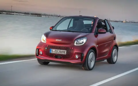 El Smart EQ Fortwo, cual es el coche más pequeño del mercado, se desplaza ágilmente por una carretera costera al atardecer.