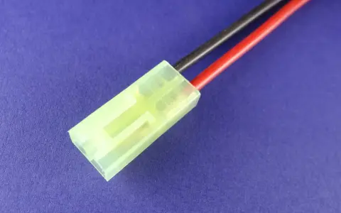 Ein gelber mini Tamiya Stecker mit roten und schwarzen Kabeln auf blauem Hintergrund.