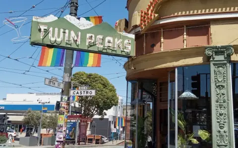 The iconic Twin Peaks sign hangs above Castro Street, a vibrant symbol of the gay area of San Francisco, adorned with rainbow flags.