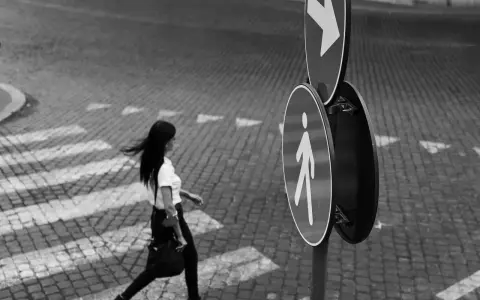 Donna attraversa la strada, un momento catturato con la street photography tecnica. Segnali stradali indicano la direzione.